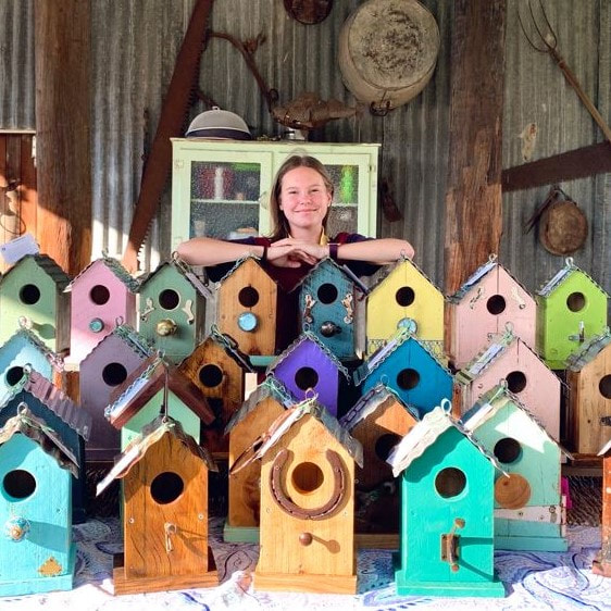 wooden coloured birdhouses and the lady who made them standing behind them