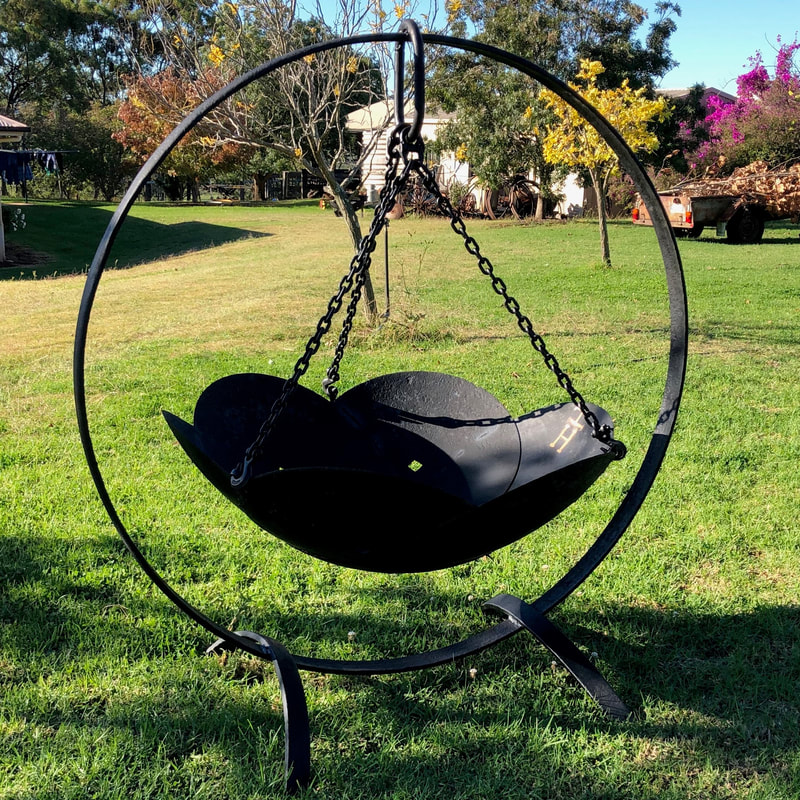 large circle of metal with a fire pit made from metal plough disks hanging from it