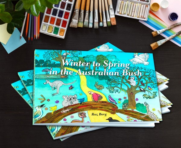 watercolour paints, brushes, pencils & pastels beside a children's book with an Australian bush scene and animals on the cover